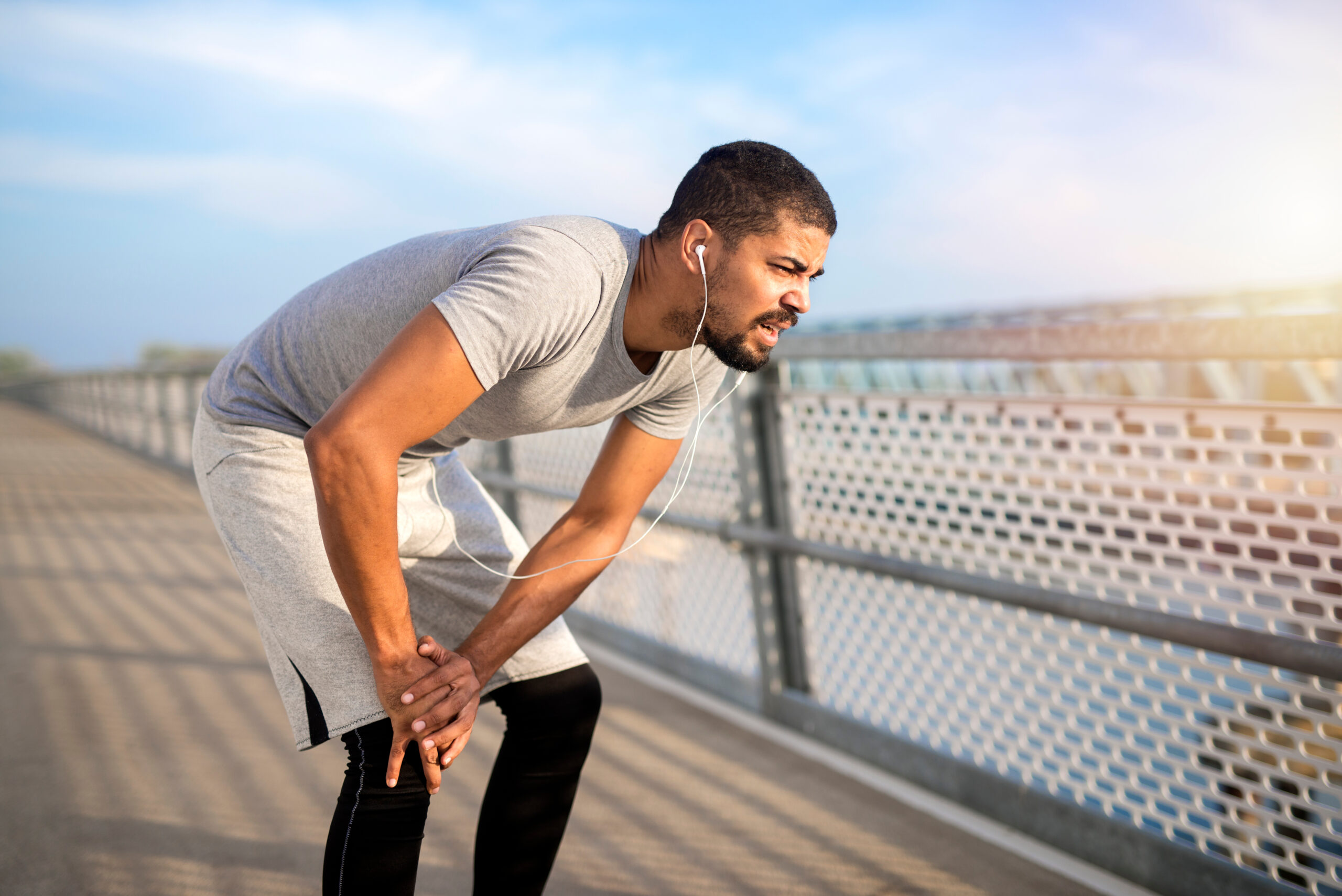 Young athlete having problem with his knee during training. Sportsman feeling pain in his knees while running. Sports injuries and health concept.