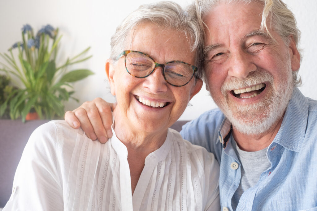 Beautiful senior couple having fun and laughing sitting at home on sofa. Serene elderly people enjoying retirement