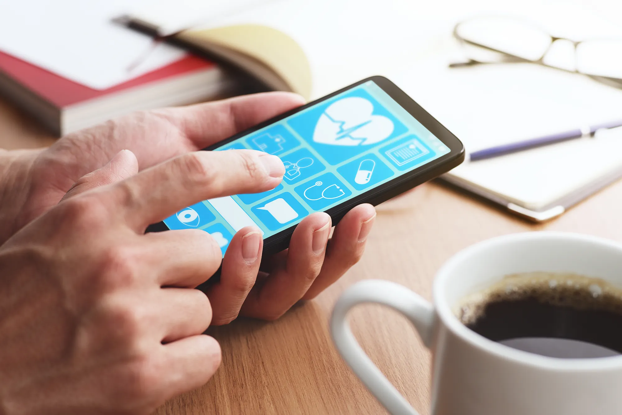 Online healthcare app on smartphone screen. Closeup of male hands touching smartphone screen at table.