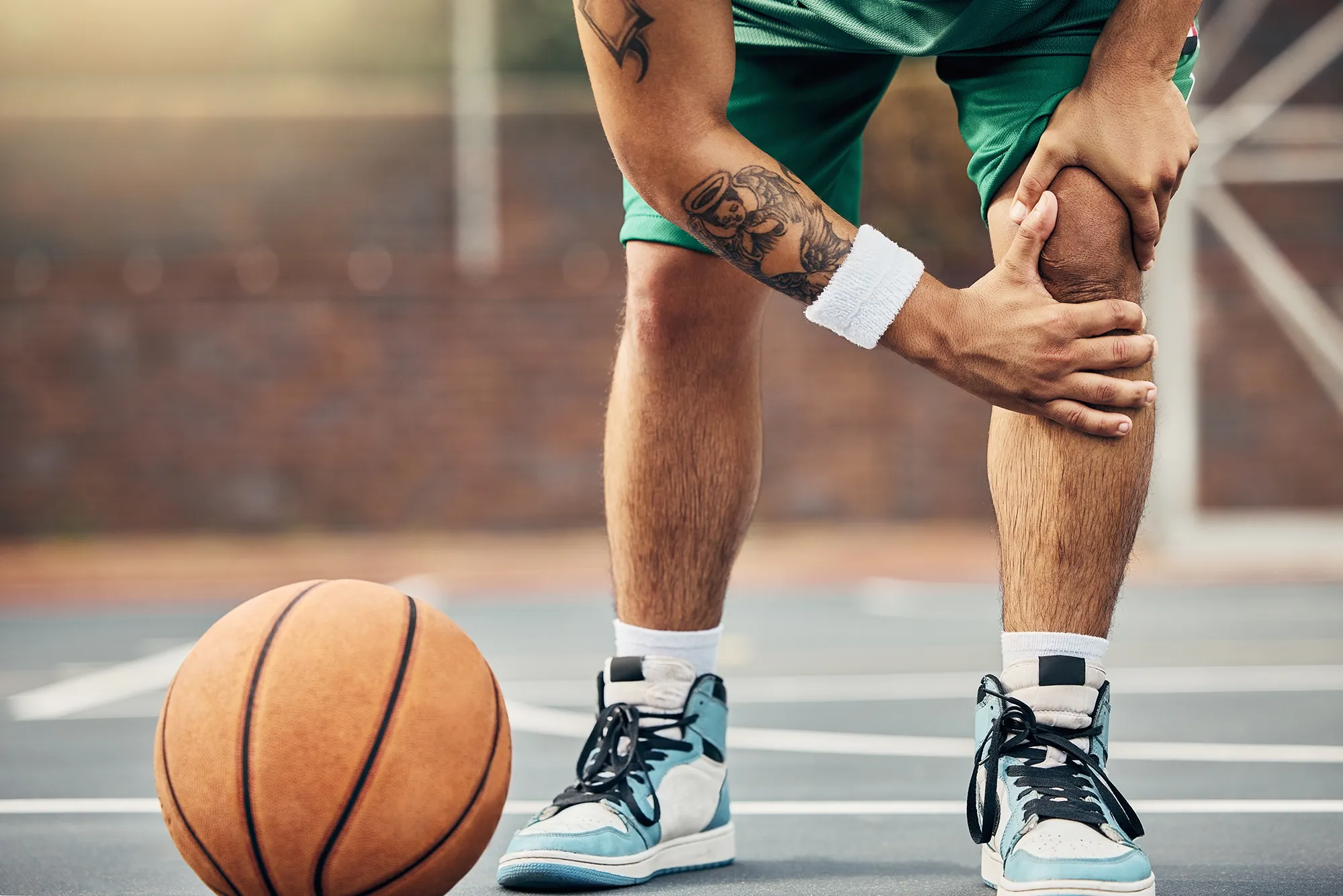 Basketball, athlete and knee injury on the basketball court during outdoor game or training. Man in with leg pain after sports accident with a broken joint, inflammation or muscle tear during match. 