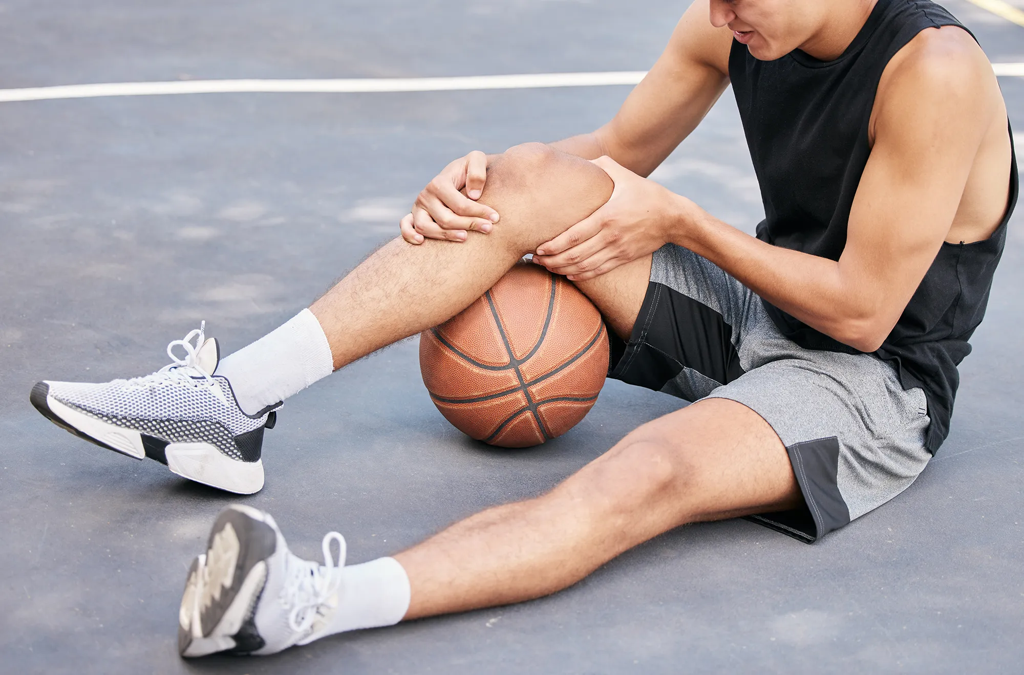 Basketball, man and knee in sports injury on the court holding painful, sore or tender area in the outdoors. Basketball player suffering from leg pain, joint or inflammation in sport match or game
