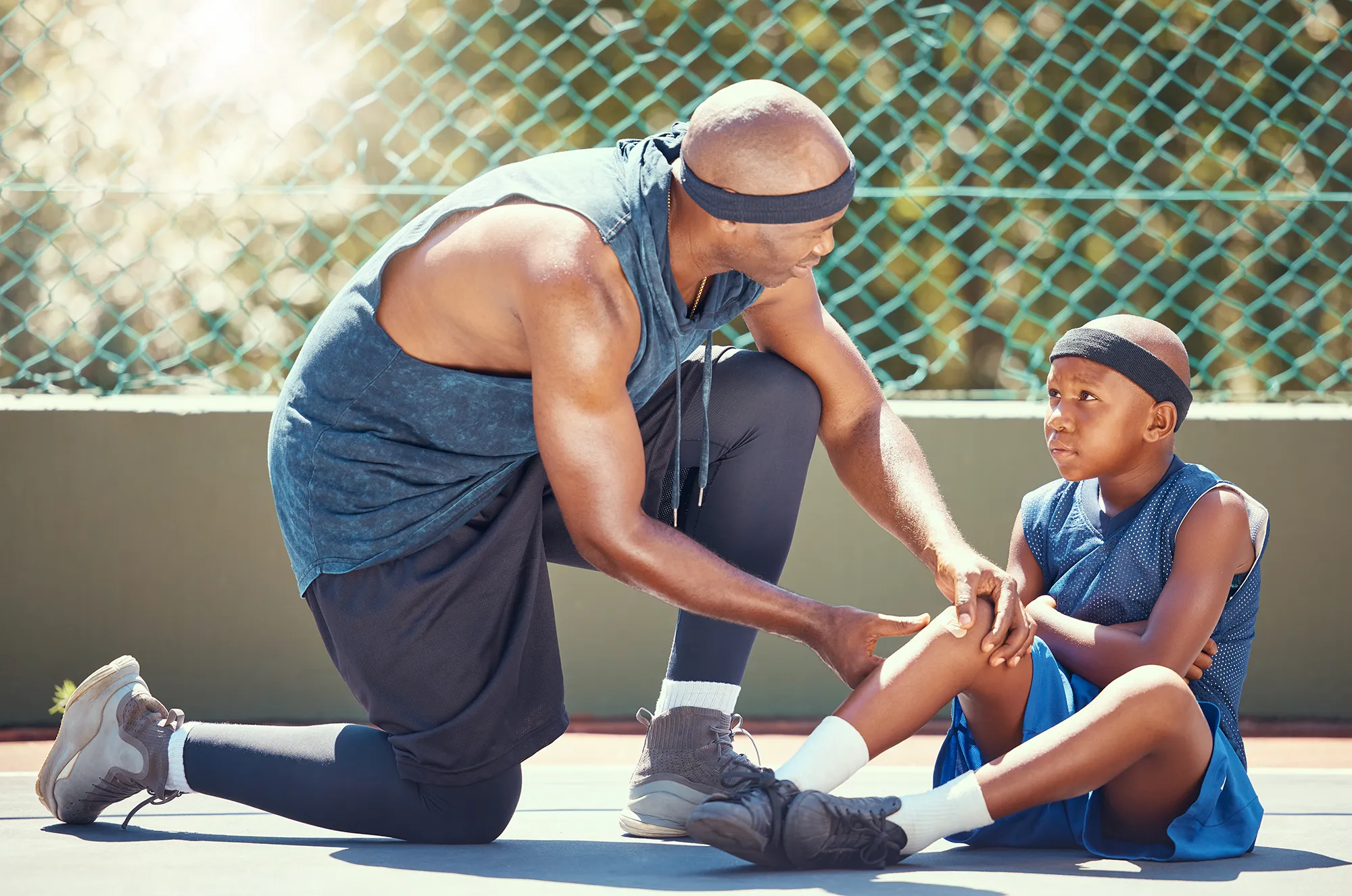 Basketball knee injury kid with dad put emergency band aid for sports training game accident at basketball court. African black father and injured child team with healing leg pain and wound plaster 