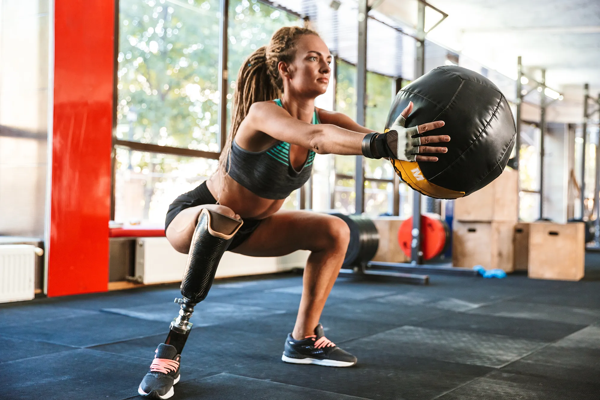 Portrait of european invalid woman with prosthesis in tracksuit, doing sit-ups with fitness ball in gym
