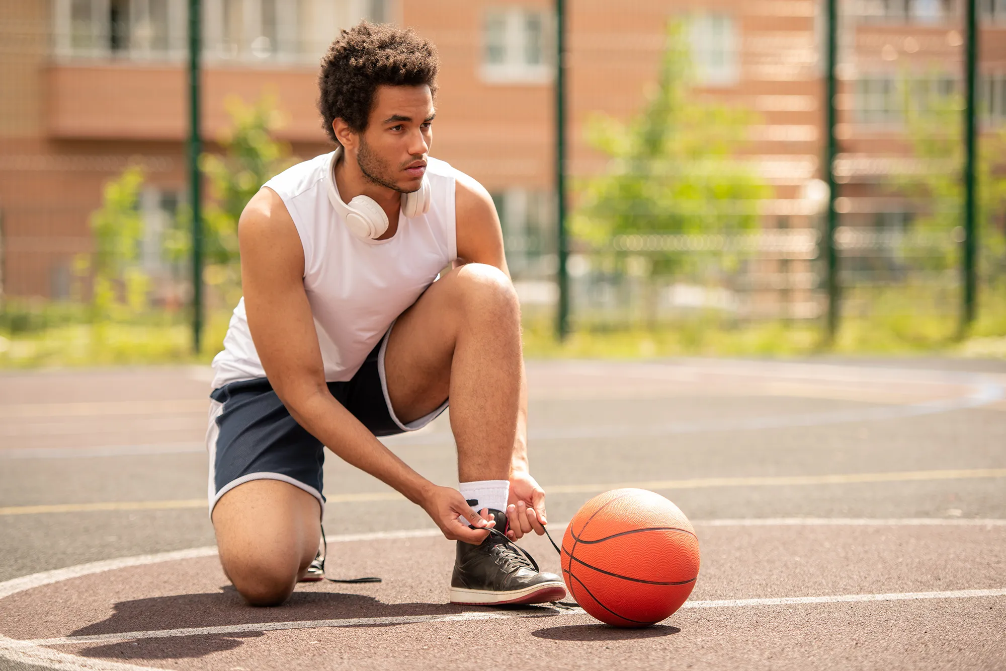 Young professional basketball player tying shoelace of sneaker
