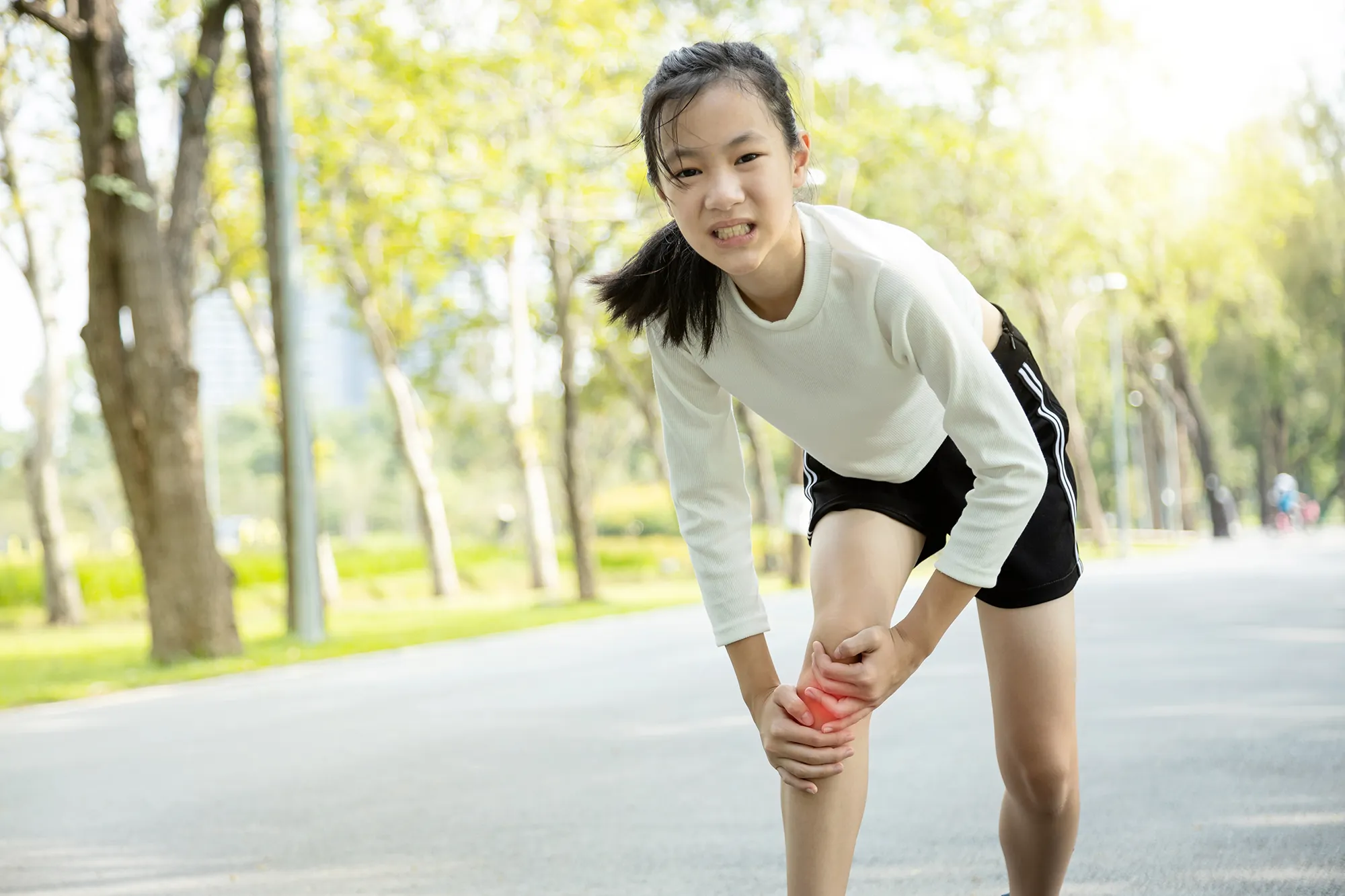 Unhappy asian child girl injured her leg pain or calf muscle while playing in sunny day, female teenage holding hands on the legs,feel pain in the knee from exercise in summer,physical injury concept 
