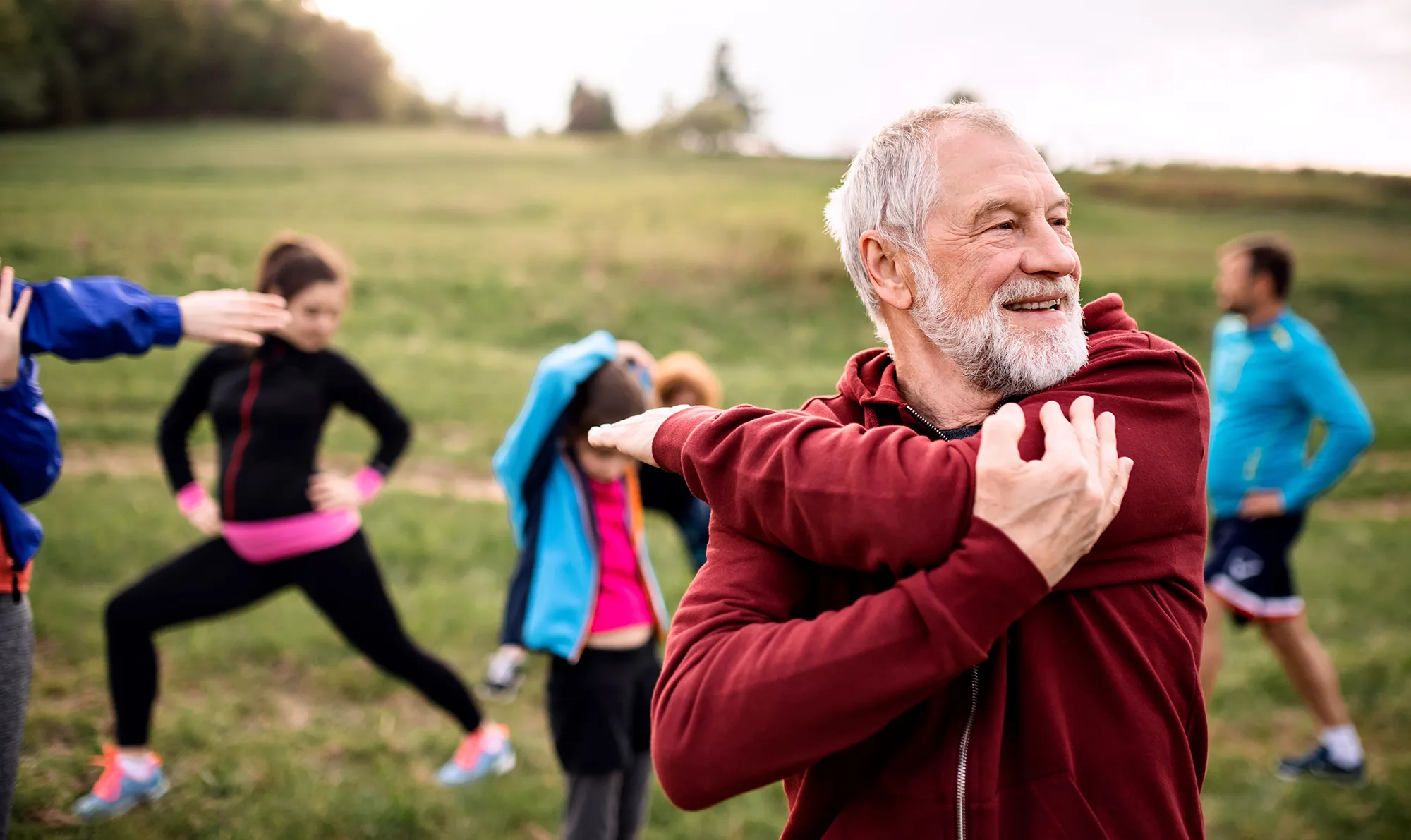 Large group of fit and active people doing exercise in nature, stretching.
