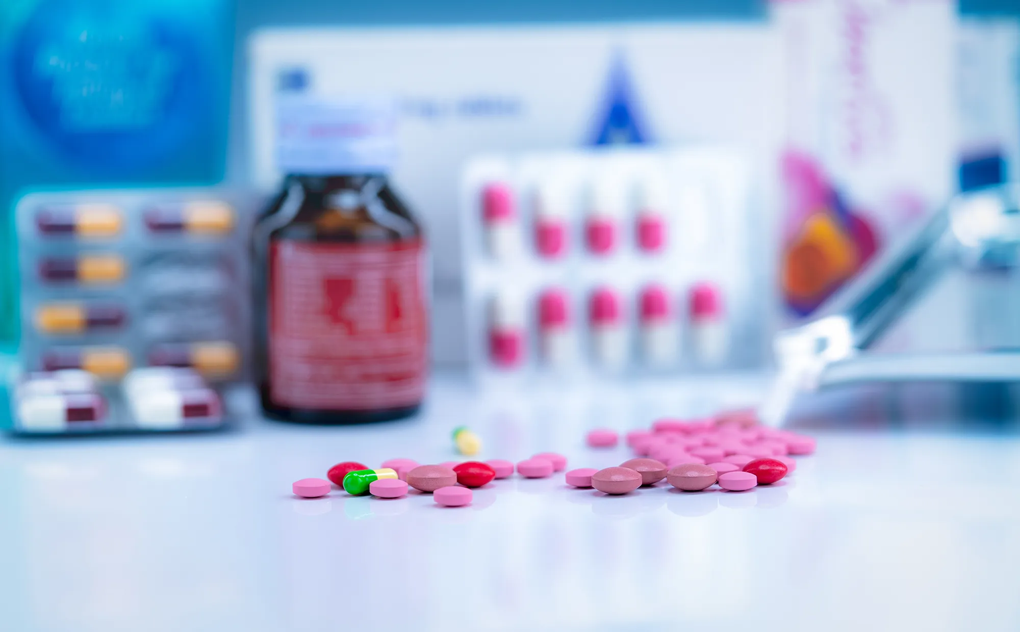 Pile of colorful tablets and capsules pills on blurred drug tray, bottle, and capsule in blister pack. Pharmacy shop background. Healthcare and drug use for treatment illness. 