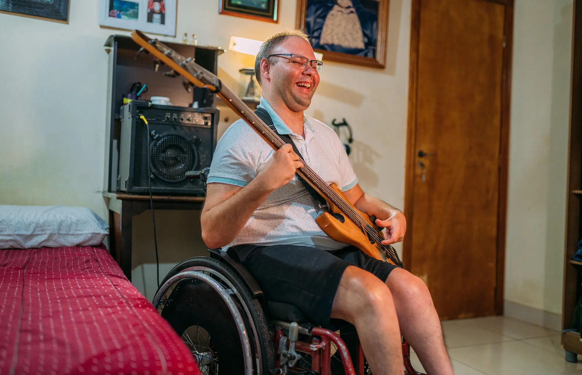 Young man using wheelchair playing on the bass guitar at bedroom
