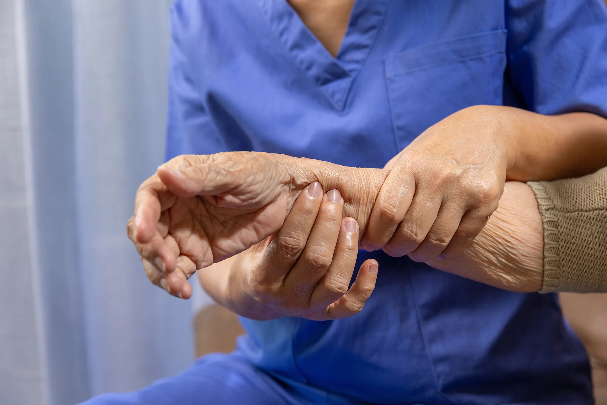 Caregiver massaging wrist of elderly woman in painful swollen gout.
