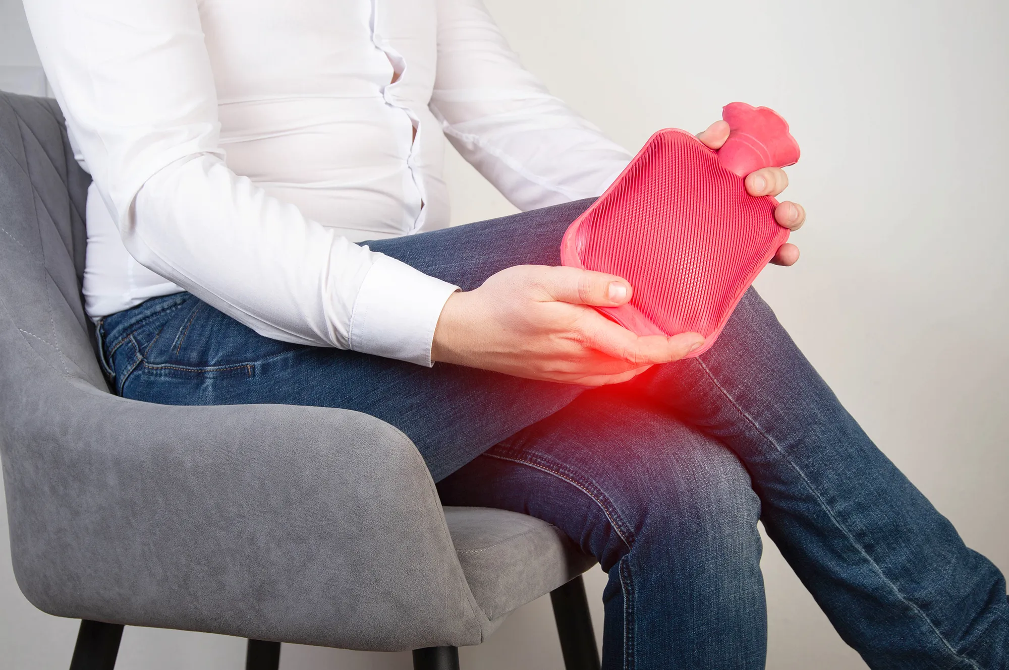 A male office worker holds a heating pad with hot water near the knee joint. Treatment of knee pain with heat therapy, rheumatoid arthritis, smooth muscle relaxation