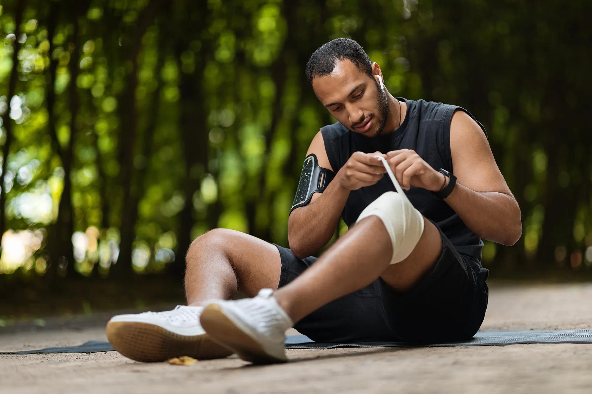 African american sportsman wrapping injured knee with elastic bandage
