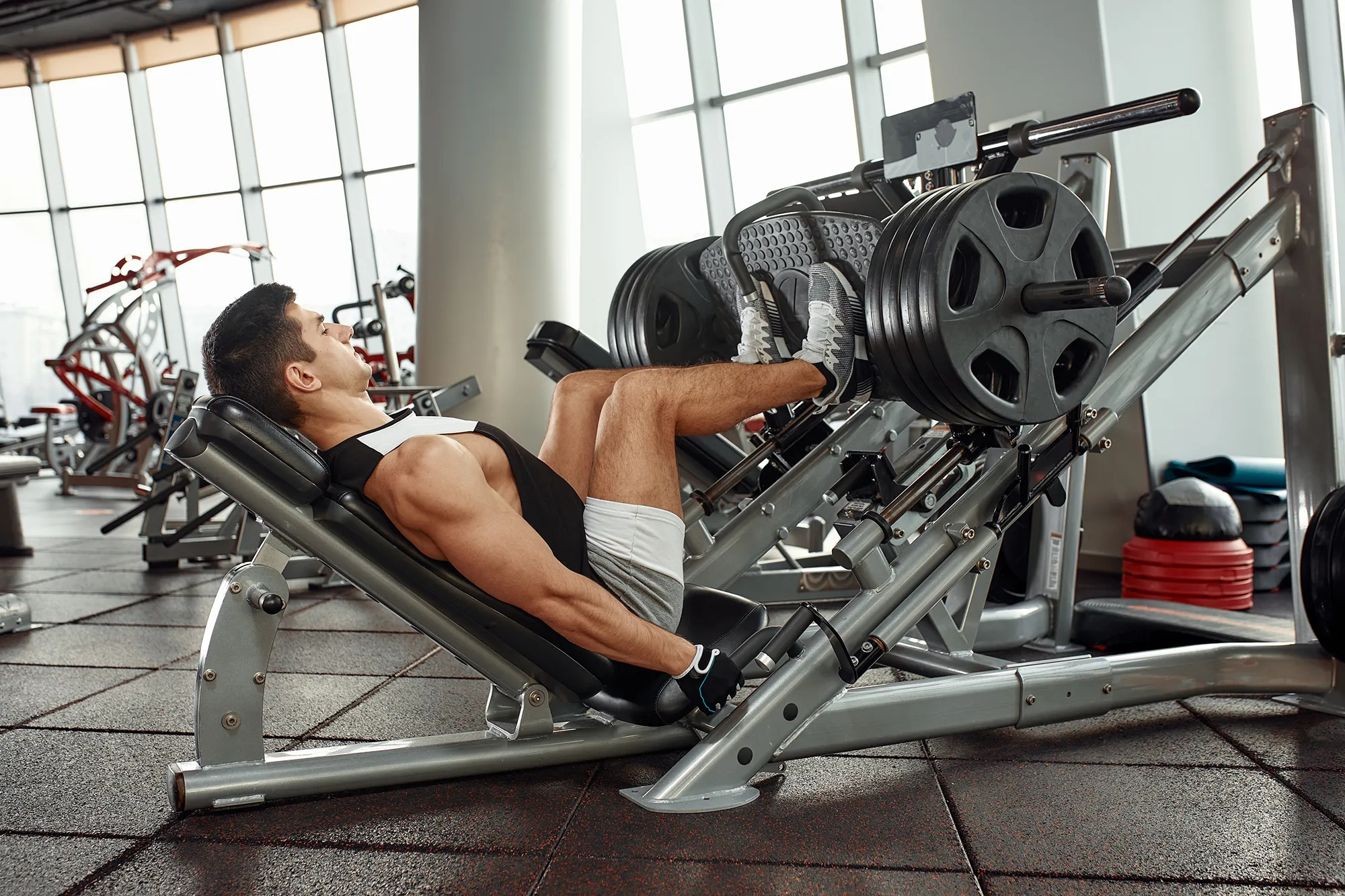 Man Using A Press Machine In A Fitness Club. Strong man doing an exercise on its feet in the simulator. Side view.
