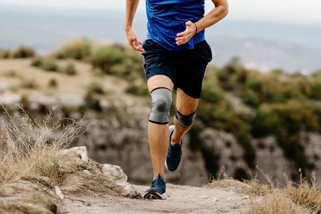 male runner with knee pads running on mountain trail, protective compression sleeves against injuries to stabilize legs
