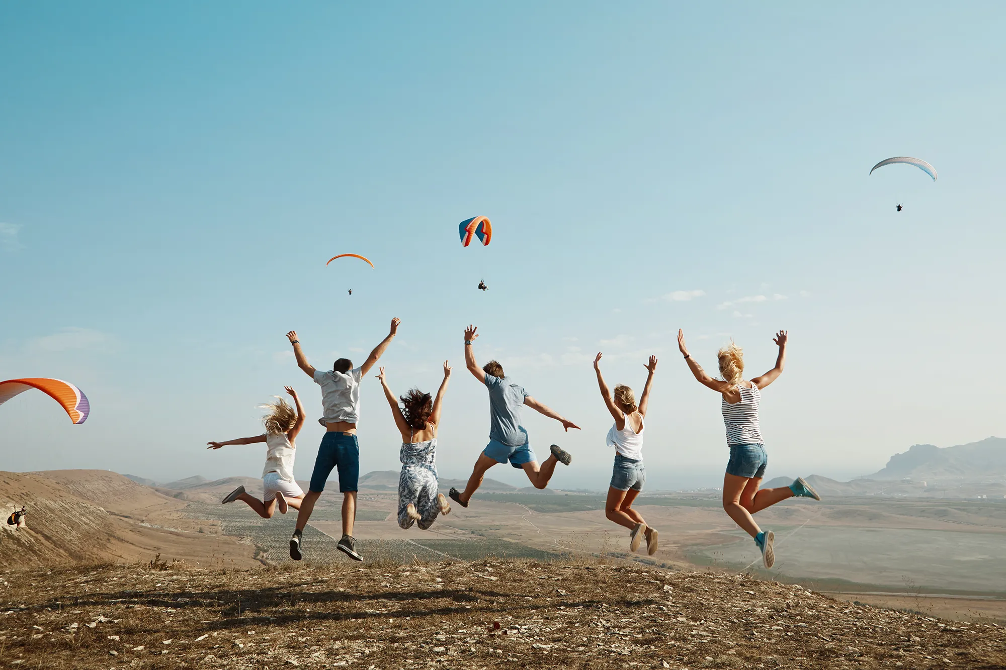 Friends joyfully jumping with glider in background.
