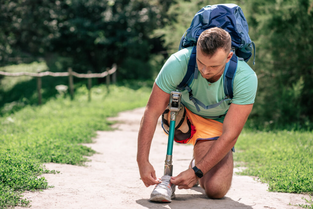 Confident pleasant man with paralysis tying his shoes while having a walk outdoors