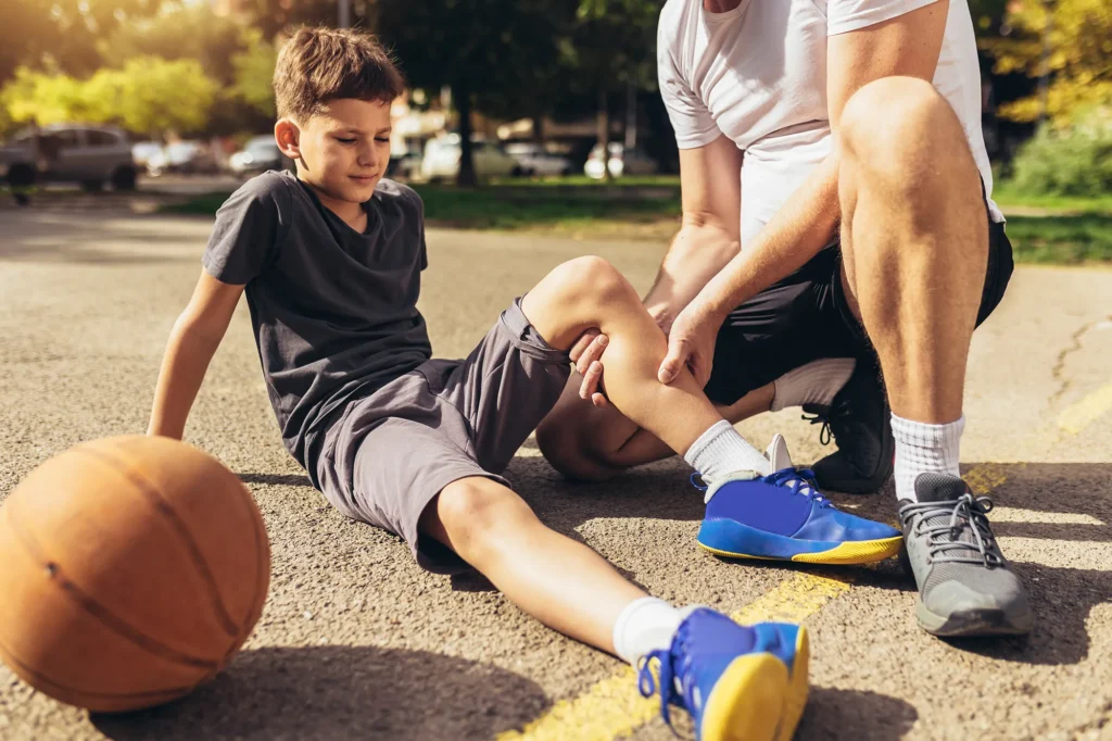 Father helping boy with knee trauma after playing basketball. Sports Injury.
